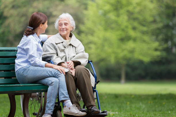 senior woman with caregiver in the park - wheelchair disabled senior adult female nurse imagens e fotografias de stock