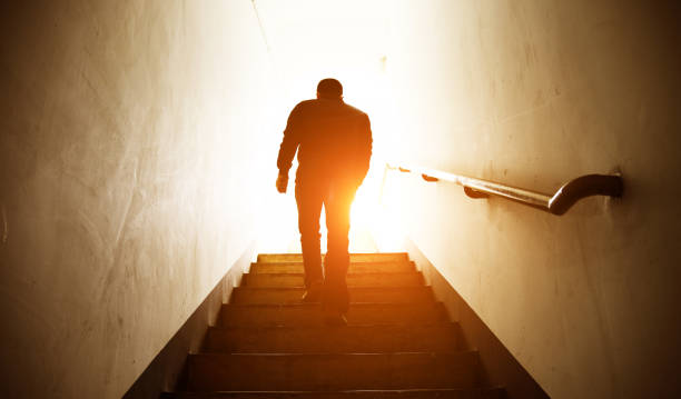 walk into the light Man walking upstairs into the light. light at the end of the tunnel stock pictures, royalty-free photos & images