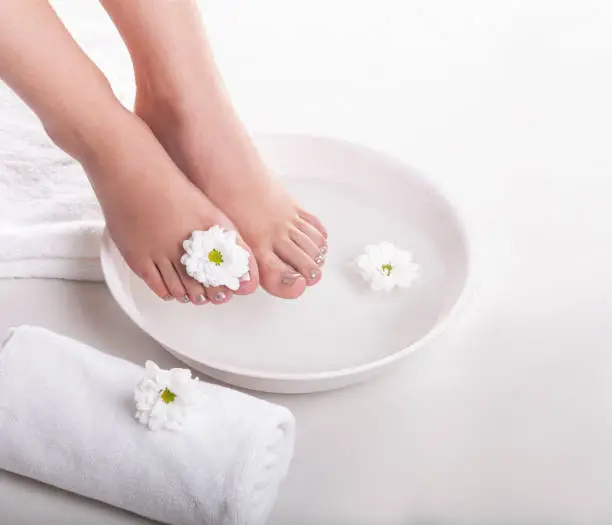 Female feet with spa bowl, towels and flowers on white background