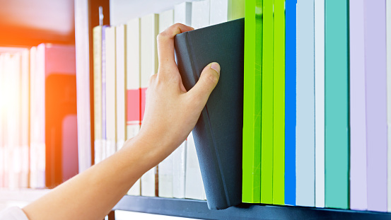 Woman hand choosing a book  from a bookshelf.