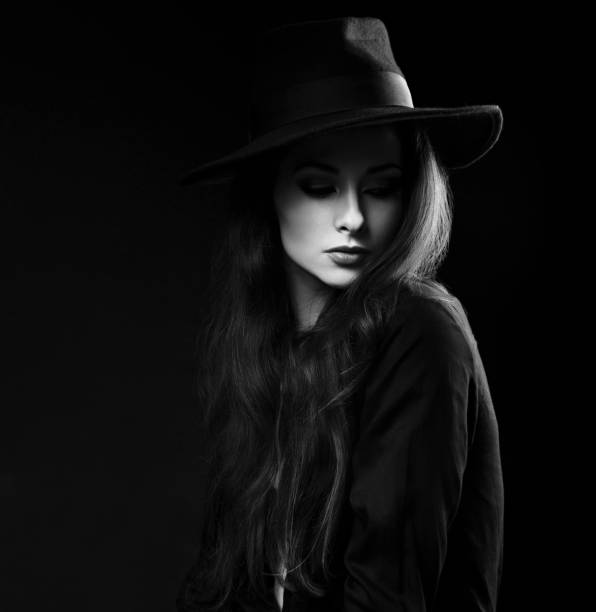 istock Expressive female makeup model posing in black shirt and elegant hat on dark background and with thinking look looking down. Dramatic light 652232590