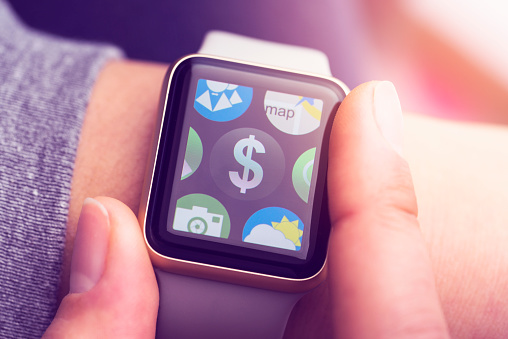 Close up shot of woman wrist wearing smart watch. Hand holding watch, banking app with dollar sign on touchscreen.
