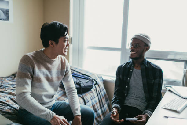 Two friends talking in a dorm room African american and asian men chatting in a dormitory room. dorm room photos stock pictures, royalty-free photos & images