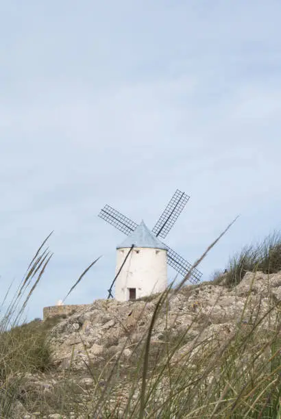 Photo of White old windmill on the hill near Consuegra (Castilla La Mancha, Spain), a symbol of region and journeys of Don Quixote (Alonso Quijano) on cloudy day.