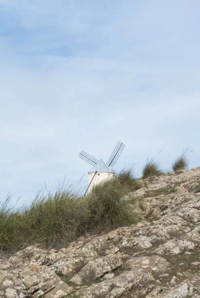 Photo of White old windmill on the hill near Consuegra (Castilla La Mancha, Spain), a symbol of region and journeys of Don Quixote (Alonso Quijano) on cloudy day.