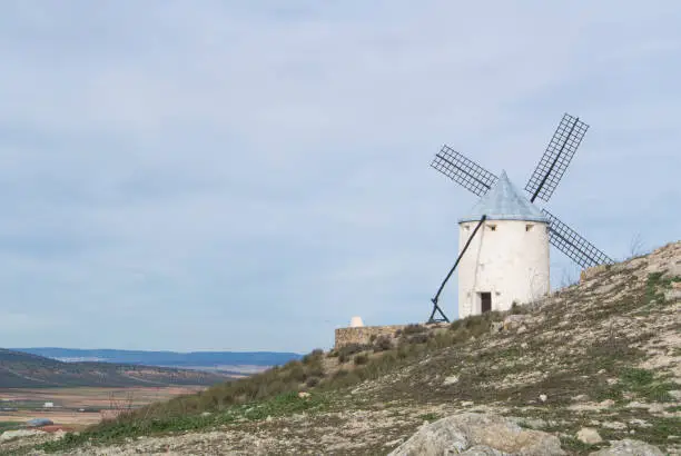 Photo of White old windmill on the hill near Consuegra (Castilla La Mancha, Spain), a symbol of region and journeys of Don Quixote (Alonso Quijano) on cloudy day.