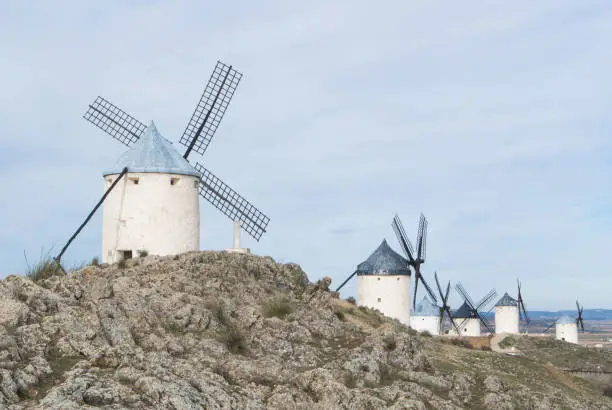 Photo of White old windmills on the hill near Consuegra (Castilla La Mancha, Spain), a symbol of region and journeys of Don Quixote (Alonso Quijano) on cloudy day.