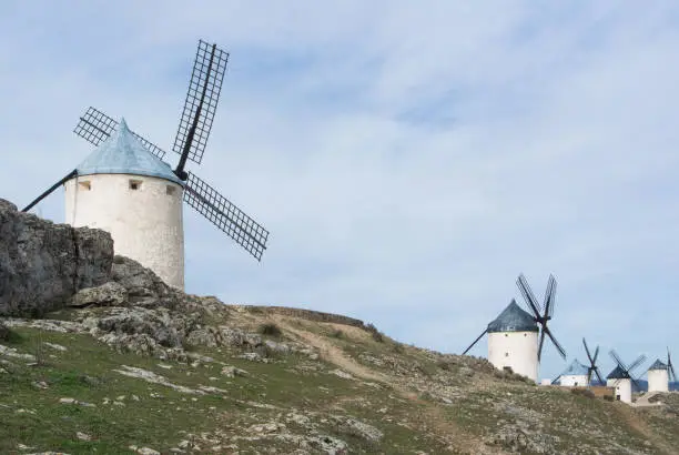 Photo of White old windmills on the hill near Consuegra (Castilla La Mancha, Spain), a symbol of region and journeys of Don Quixote (Alonso Quijano) on cloudy day.