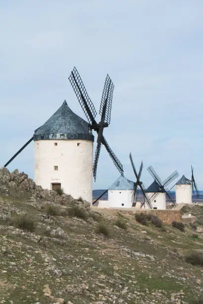 Photo of White old windmills on the hill near Consuegra (Castilla La Mancha, Spain), a symbol of region and journeys of Don Quixote (Alonso Quijano) on cloudy day.