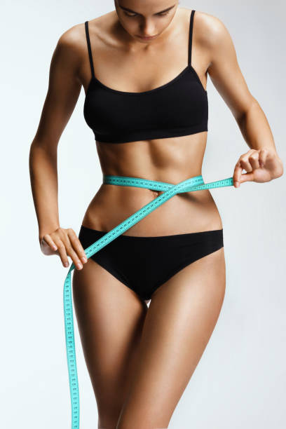 Slim girl in black lingerie with a ribbon measures the size of the waist stock photo