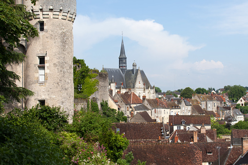 Horizontal landscape photo of the cobblestone paved walkway leading to the former drawbridge entrance in the surrounding wall of the castle at Saumur. Trees, Castle towers and rooftops can be seen in the distance under a blue sky. Saumur, Maine-et-Loire, France. 1st April, 2019