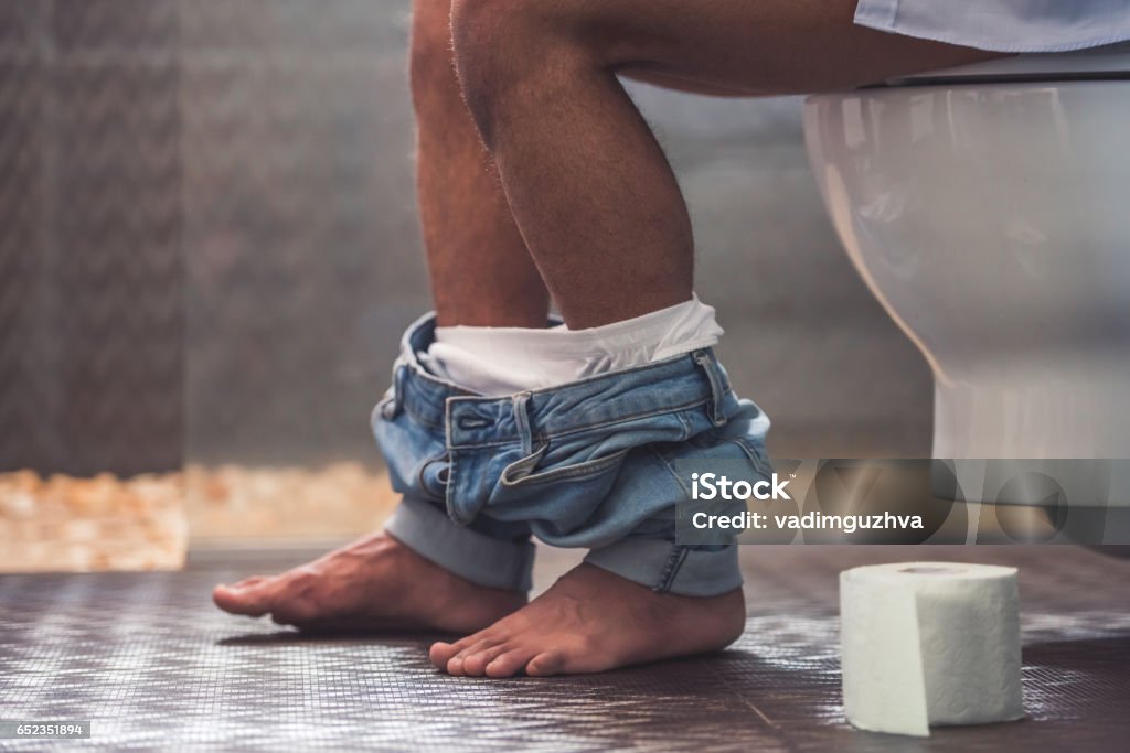 Afro American man in toilet Cropped image of handsome Afro American man sitting on toilet. His jeans is hanging on his legs Toilet Stock Photo