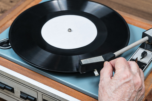 Wrinkled hand of an elderly woman puts the needle on the disc on retro vinyl player, close-up