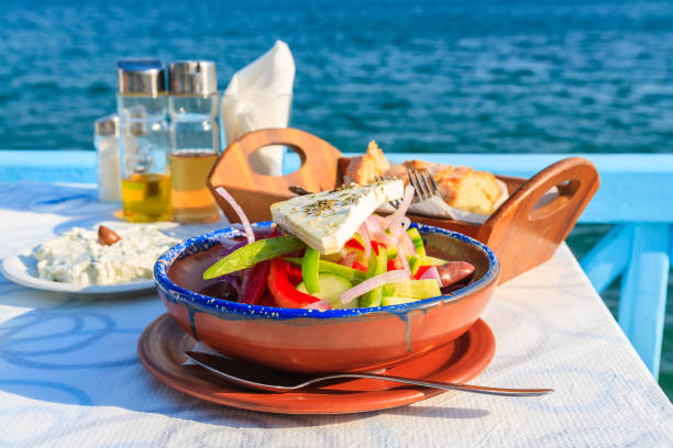 insalata greca in tavola nella taverna greca con acqua di mare blu sullo sfondo, isola di samos, grecia - greek cuisine greek culture food table foto e immagini stock