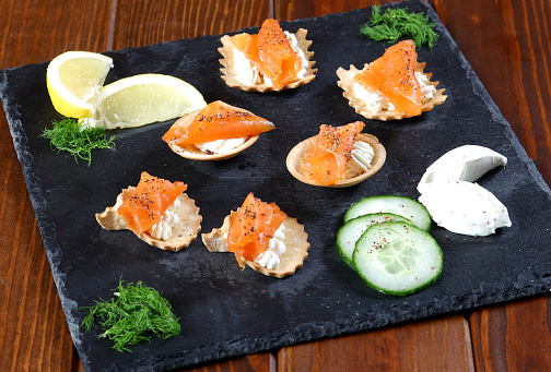 Salmon Delight, on slate board, with biscuit filled with cream cheese, and cucumber garnish. Fresh lemon over top, sprinkle with black peppers and chili pepper garnish.