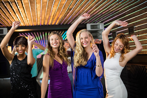 Group of smiling friends dancing on dance floor in bar