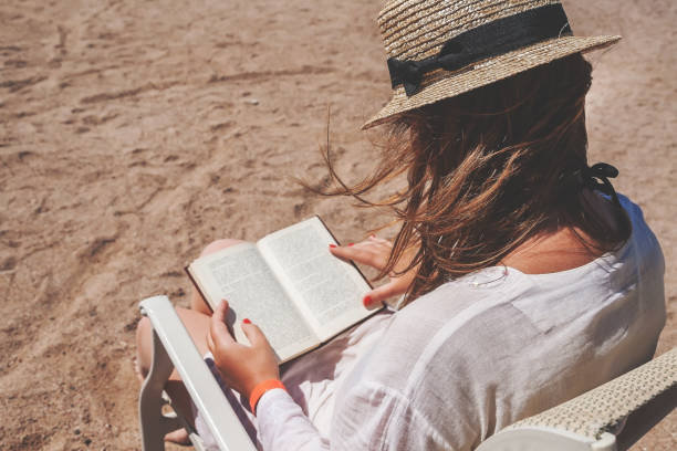 istock Young adult woman with a hat on the beach reading a book 652423402