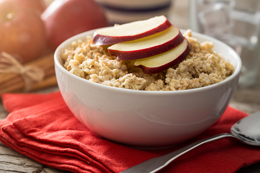 Apple and cinnamon oatmeal for breakfast on rustic wood farm table with apples and cream.