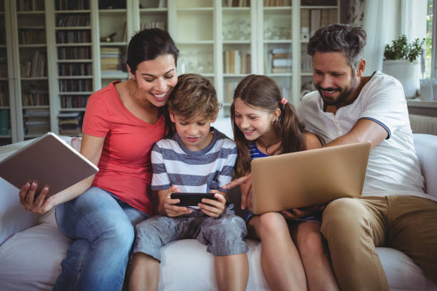 glückliche familie auf sofa sitzen und mit laptop, handy und digital-tablette - wohnanlage stock-fotos und bilder