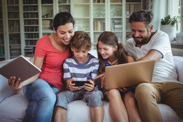 Happy family sitting on sofa and using laptop, mobile phone and digital tablet