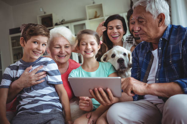happy multi-generation family using digital tablet in living room - wireless technology cheerful granddaughter grandmother imagens e fotografias de stock