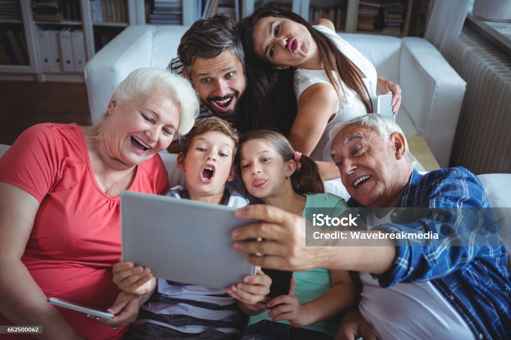 Multi-generation family taking a selfie on digital tablet in living room Multi-generation family taking a selfie on digital tablet in living room at home Family Stock Photo
