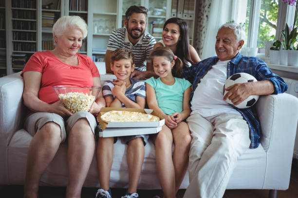 mehr-generationen-familie sitzt mit popcorn und pizza beim fußballspiel ansehen - grandmother senior adult child multi generation family stock-fotos und bilder