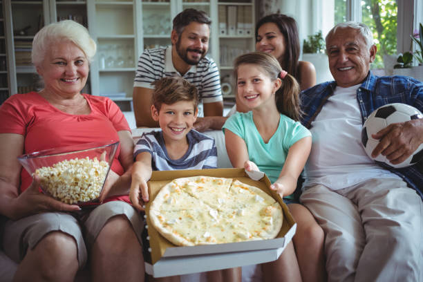 mehr-generationen-familie sitzt mit popcorn und pizza beim fußballspiel ansehen - grandmother senior adult child multi generation family stock-fotos und bilder