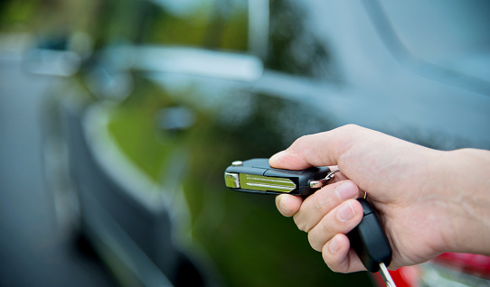 Woman unlocking a car by pressing on the remote control car alarm systems.