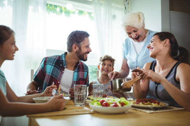 starsza kobieta serwująca posiłek swojej rodzinie - dining table child grandparent grandchild zdjęcia i obrazy z banku zdjęć