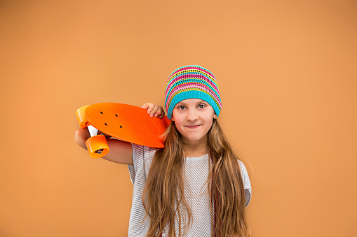 Pretty skater girl holding skateboard on blue studio background