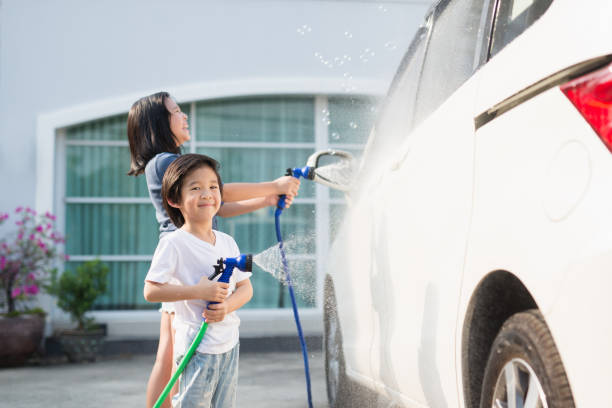 Asian children washing car in the garden on summer day
