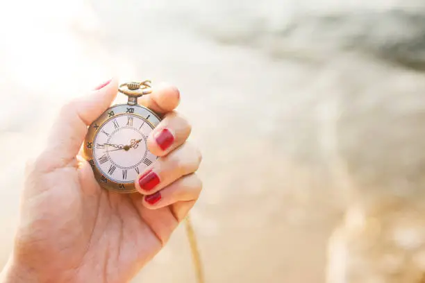 Vintage pocket watch in woman hand in sunrise or sunset, sea as background, Time and Aging concept