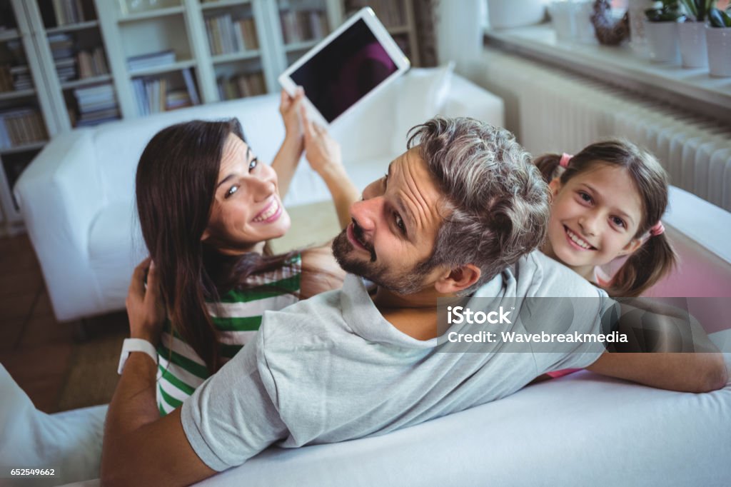 Parents sitting on sofa with daughter and clicking a selfie on digital tablet Parents sitting on sofa with daughter and clicking a selfie on digital tablet at home Digital Tablet Stock Photo