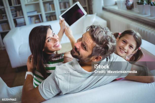 Parents Sitting On Sofa With Daughter And Clicking A Selfie On Digital Tablet Stock Photo - Download Image Now