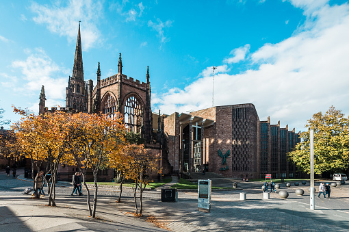 Coventry, England - October 23, 2016: people are walking on the street and passing by the runied Cathedral Church of St Michael in Coventry, England