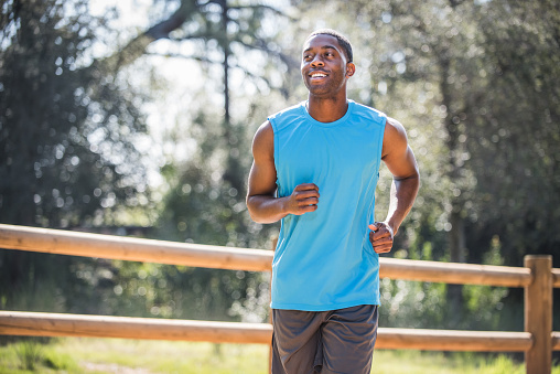 African American young adult male running on a dirt trail.