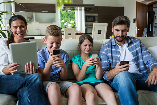 Family using laptop and mobile phone in living room at home