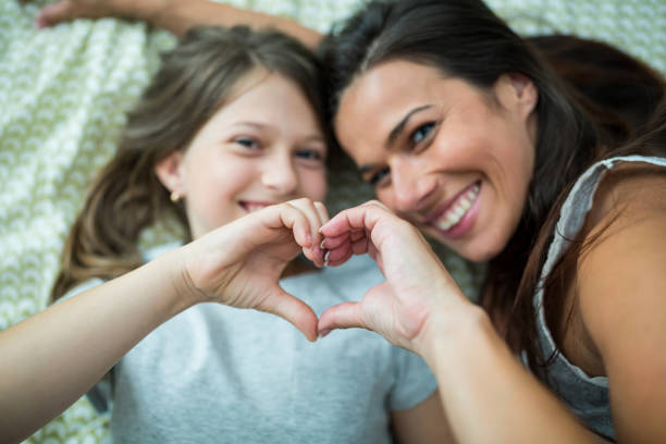 istock Mother and daughter making heart shape from hand while lying on bed 652632584
