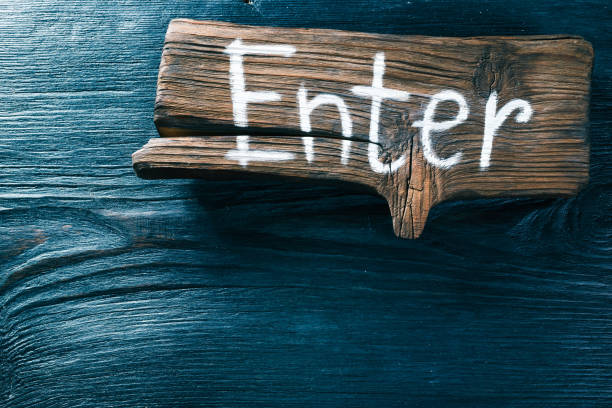 Brown textured wood signboard with text 'Enter' on black wood surface. Top view