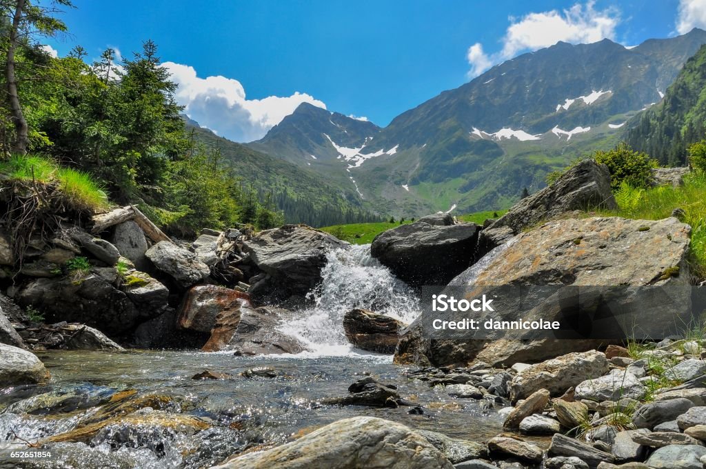 View from Romanian Carpathian Mountains- Mountain summit and river valley Scenic landscape of snowy mountain in the background and a small waterfall in the foreground Carpathian Mountain Range Stock Photo