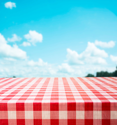 It's time for spring and summer picnics.  A red checked tablecloth with beautiful cloudy sky defocused in background.  Empty table is perfect space for your object placement.
