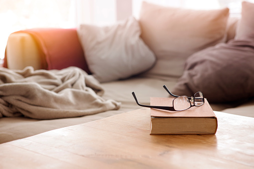 book with eyeglasses on wooden table in front of cozy couch