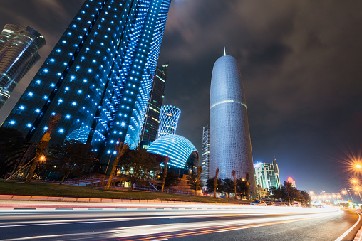 Futuristic modern skyscrapers illuminating the night at the famous corniche street and promenade with motion blured traffic lights in the capital city of Doha, Qatar, Middle East.