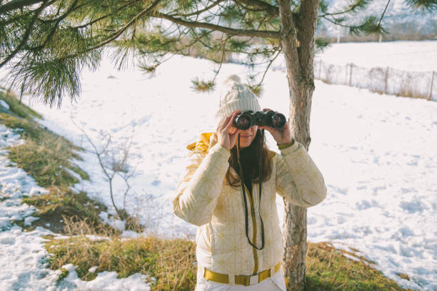istock The girl in a White cap with a backpack in the winter in a forest looking through binoculars 652764998
