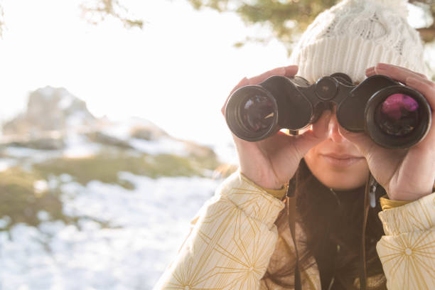 istock The girl in a White cap with a backpack in the winter in a forest looking through binoculars 652765116