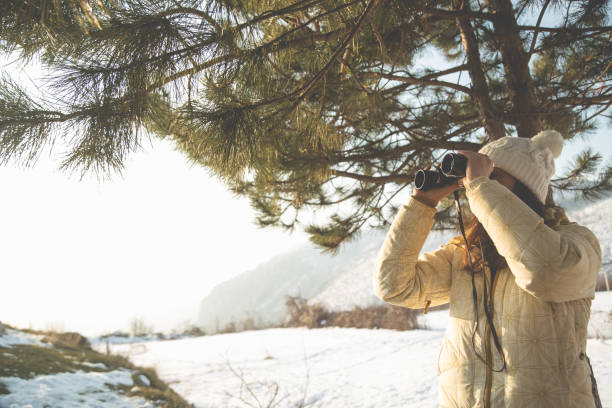 istock The girl in a White cap with a backpack in the winter in a forest looking through binoculars 652765160