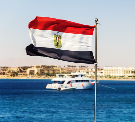 The flag of Egypt evolves against the backdrop of a yacht and the sea.