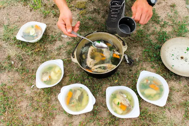 A man spills a soup cooked in nature from a fish. Outdoor kitchen. Outdoor food.