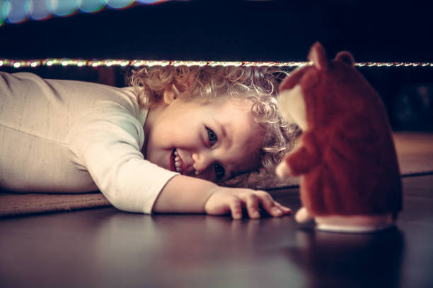 lustige süße lächelnde baby spielen verstecken und suchen unter dem bett mit spielzeug hamster im vintage-stil - child discovery surprise playing stock-fotos und bilder
